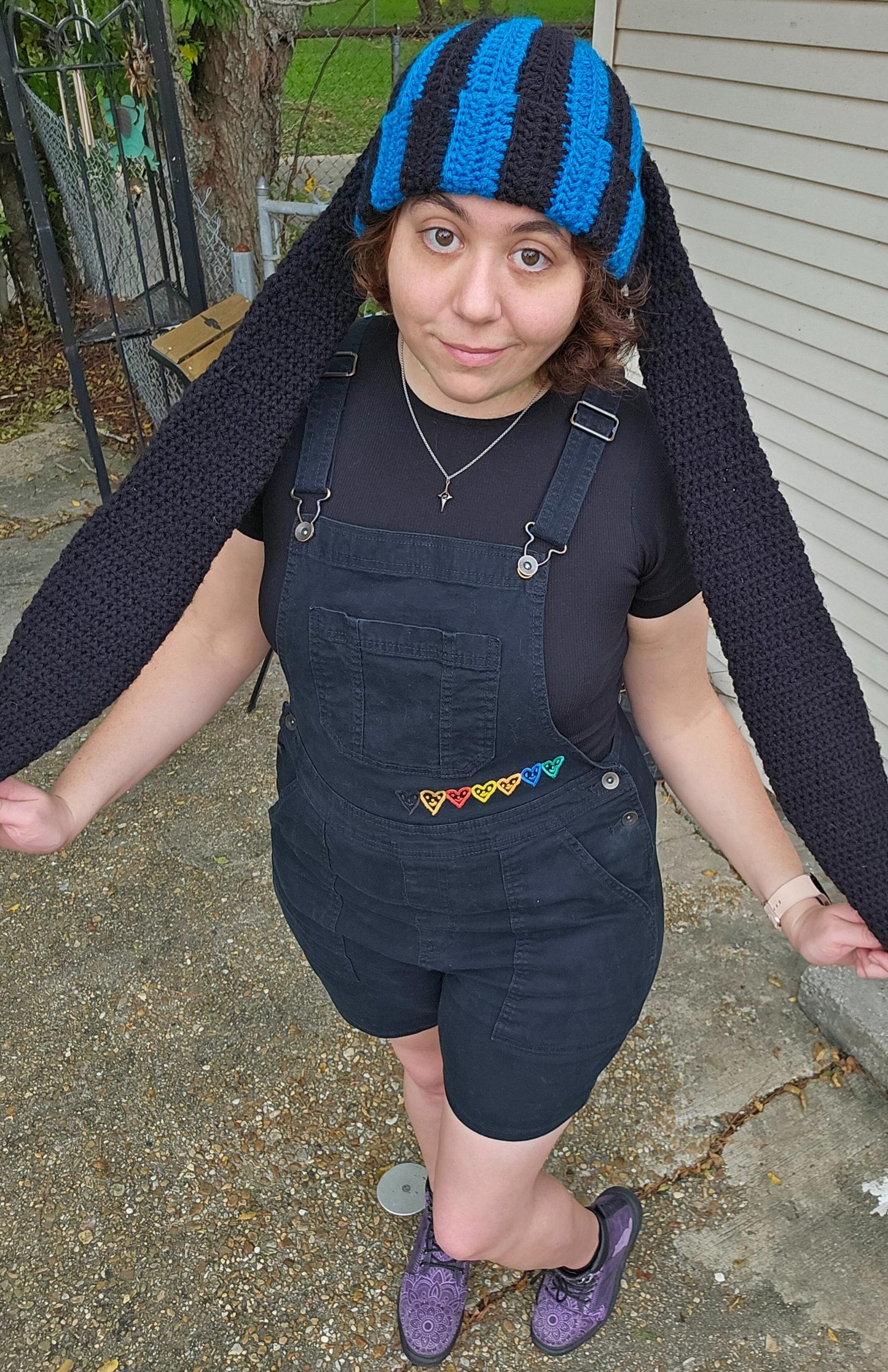 The image features a crocheted beanie with extra long bunny ears in a black and sapphire blue striped pattern. The ears are stretched to their max length.