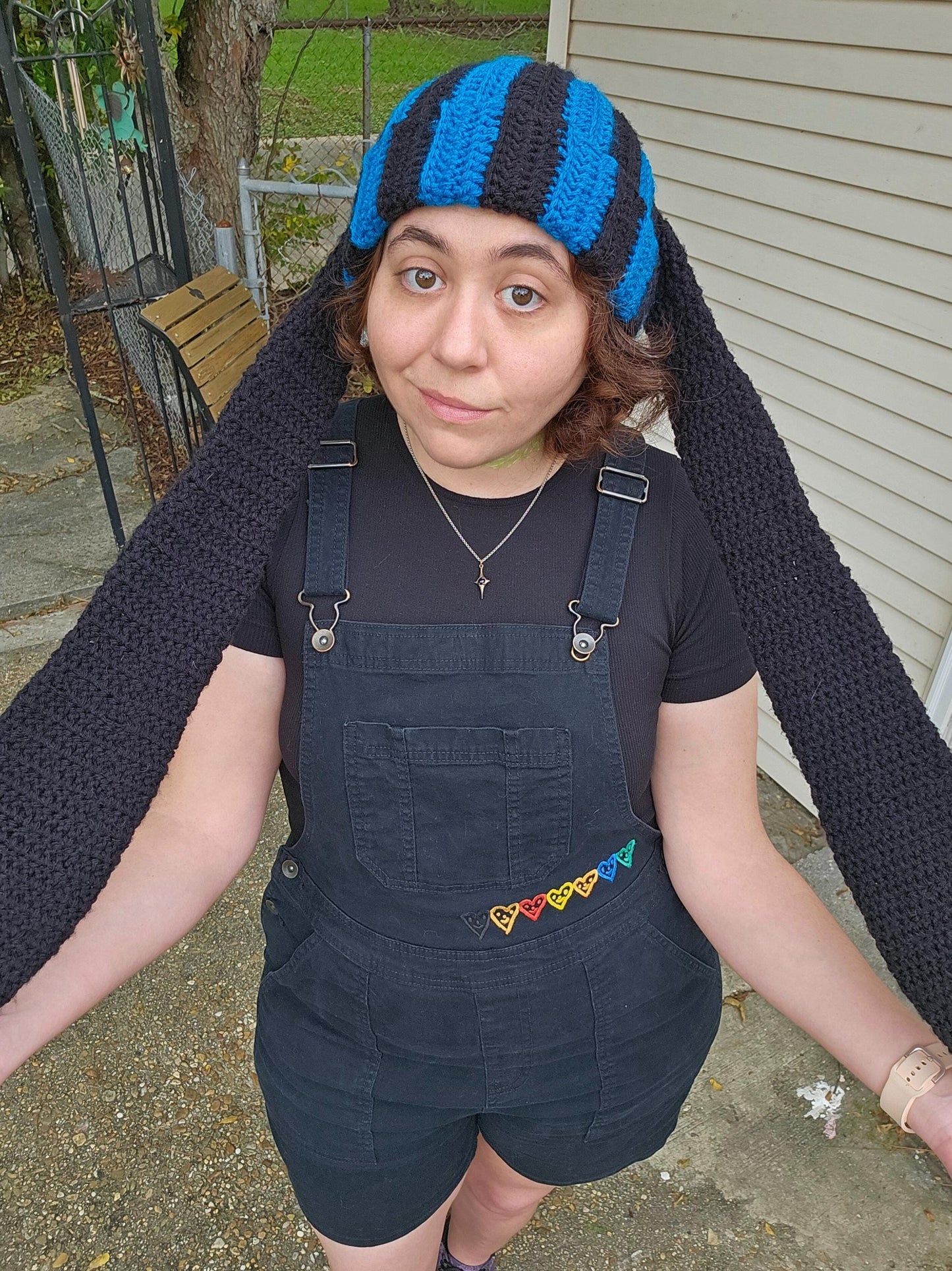 The image features a crocheted beanie with extra long bunny ears in a black and sapphire blue striped pattern. The ears are stretched to their max length.