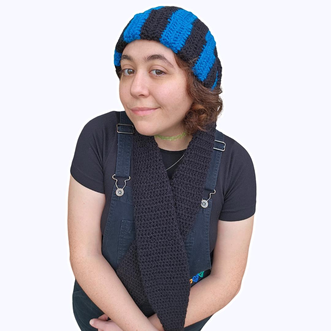 The image features a crocheted beanie with extra long bunny ears in a black and sapphire blue striped pattern. The ears are crossed in front of the wearer.