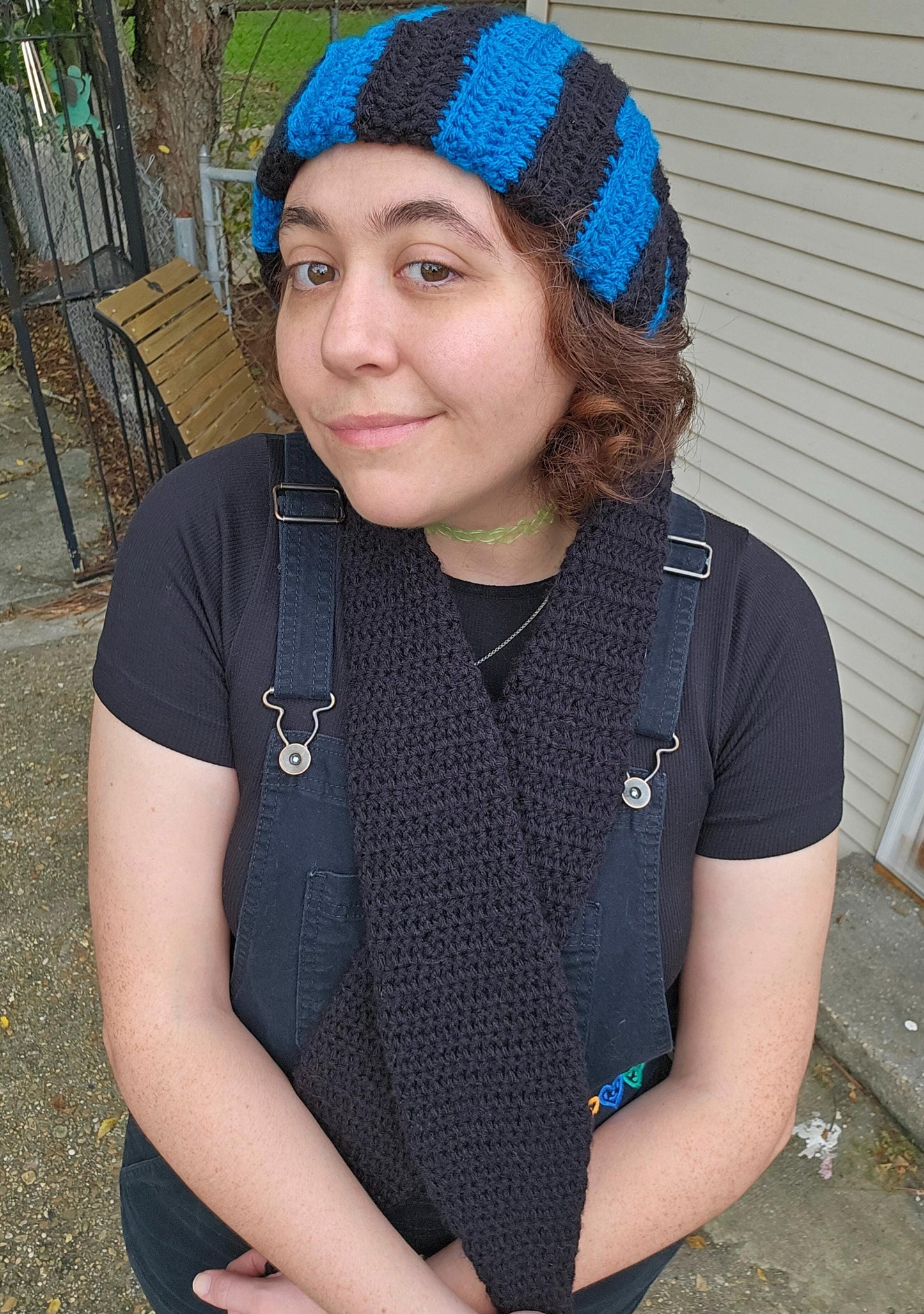 The image features a crocheted beanie with extra long bunny ears in a black and sapphire blue striped pattern. The ears are crossed in front of the wearer.