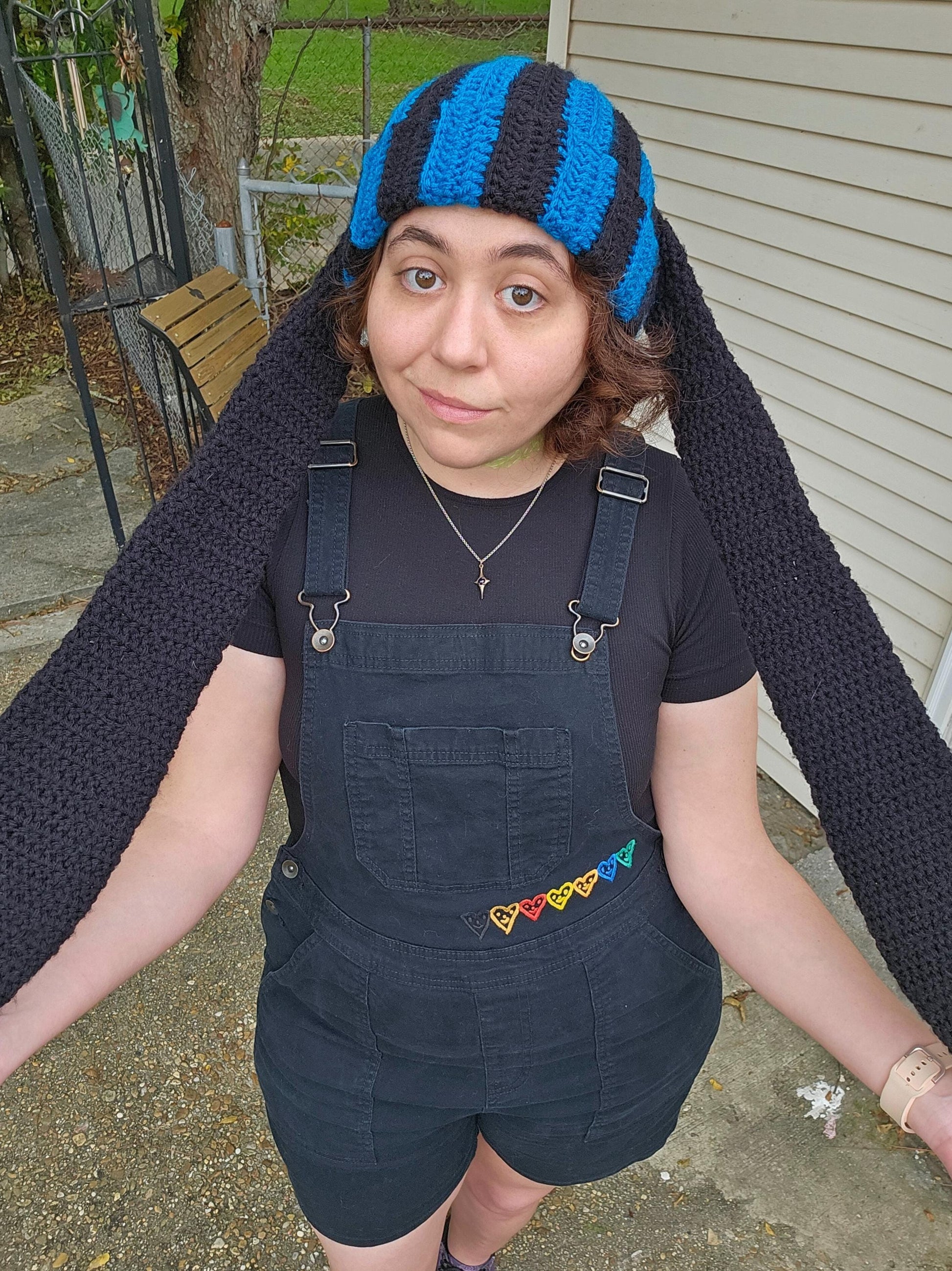 The image features a crocheted beanie with extra long bunny ears in a black and sapphire blue striped pattern. The ears are stretched to their max length.